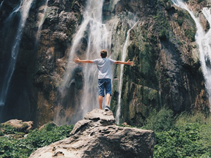 Young person standing in front of a waterfall. Arms spread to the side. Meant to illustrate praise to the Lord