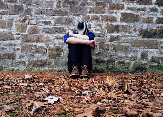 Man sitting against a brick wall with his head resting on his knees. Meant to illustrate our sadness when we quench the work of the Holy Spirit in our lives.